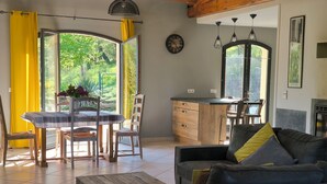 A modern living room with a sofa, coffee table, dining table, chairs, and a kitchen area with a sink and cabinets.