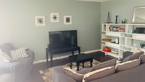 A living room with a flat-screen TV, a sofa, a coffee table, and a bookshelf. - Charming 2-bedroom cottage with WiFi, AC in fabulous Elk Rapids (Elk Rapids)