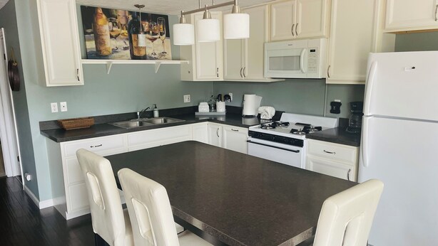 A modern kitchen with white cabinets, a dark countertop, a built-in oven, and a refrigerator. There is a dining area with a table and chairs. - Charming 2-bedroom cottage with WiFi, AC in fabulous Elk Rapids (Elk Rapids)