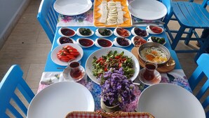 A table set for a meal with various dishes, including bread, salads, and dips, on a balcony with blue chairs. - ADA LUNA BOZCAADA (Bozcaada)