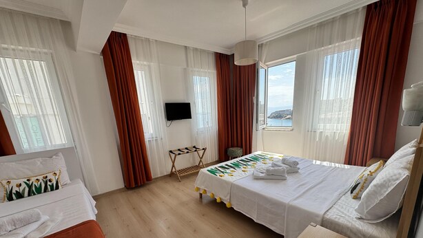 A hotel room with a bed, a desk, a TV, and a window with curtains. - ADA LUNA BOZCAADA (Bozcaada)
