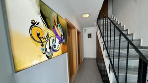 A hallway with a staircase, a wall with a colorful abstract painting, and patterned floor tiles. - ADA LUNA BOZCAADA (Bozcaada)