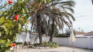 A courtyard with a palm tree, white umbrellas, and a stone-paved area. - Typical  ibiza-style family villa with large swimming pool 15 mn from Sitges (Cunit)
