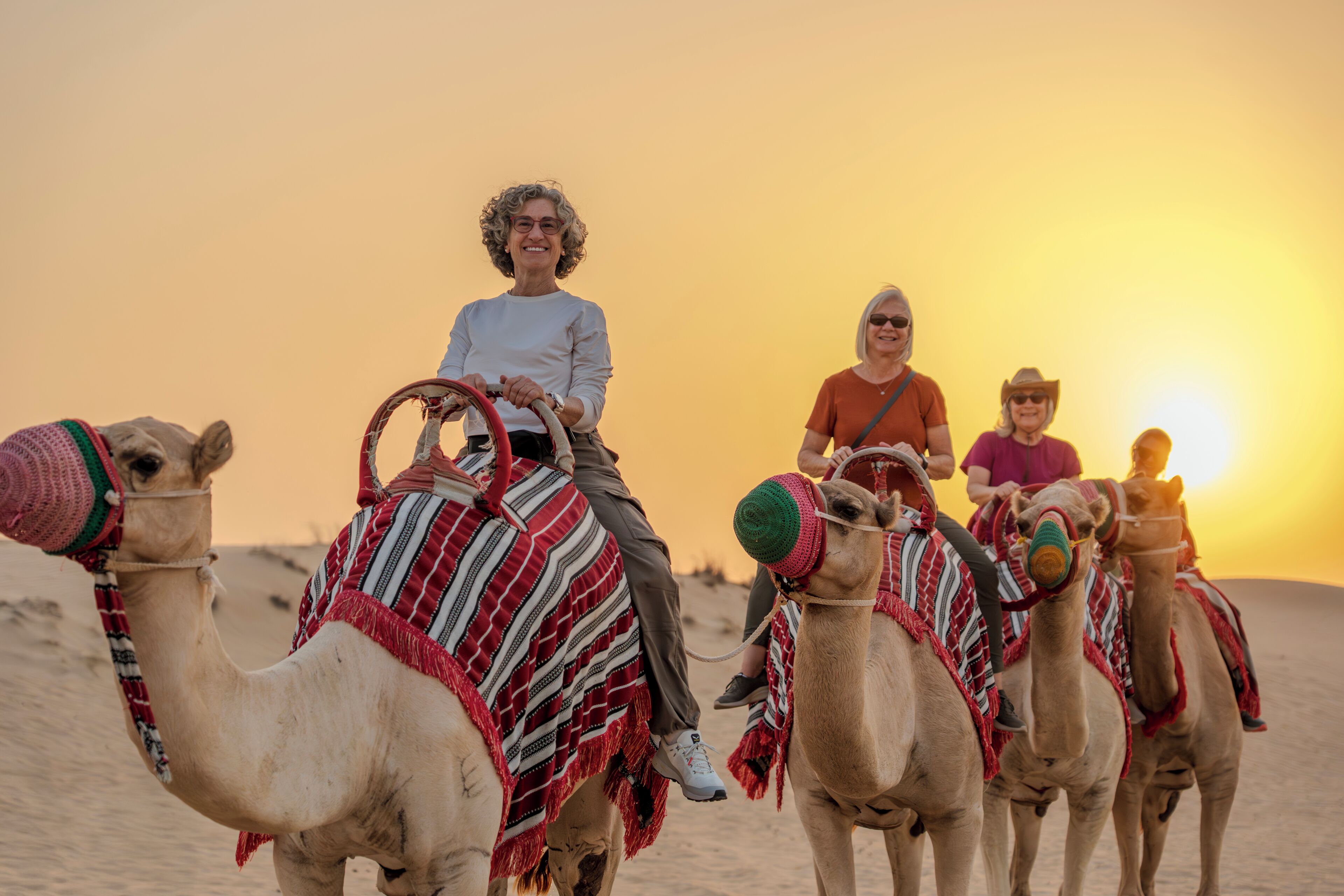 Cena de deserto com camelos e pessoas montadas neles.
