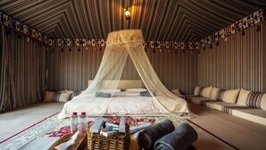 Una habitación con una cama, un sofá, una cama con dosel, una pared con diseño y un techo con lámpara.