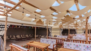 Un espacio al aire libre con mesas y bancos de madera, piso con diseño y un escenario con cortinas.