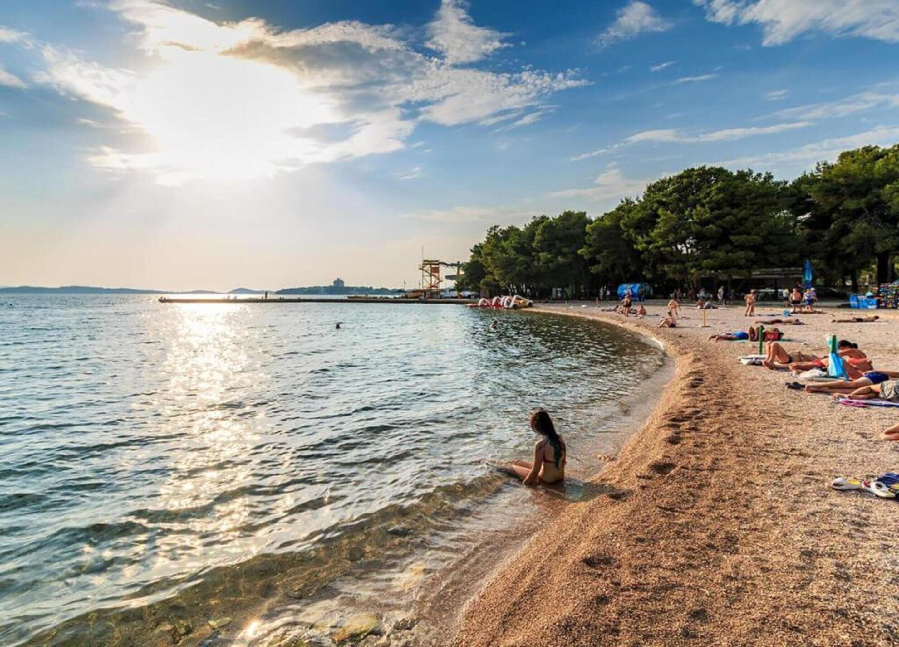 A beach with clear water, a lifeguard tower, and people sunbathing.