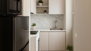 Una cocina moderna con un refrigerador negro, gabinetes blancos, un protector contra salpicaduras de mármol y un lavamanos de acero inoxidable.