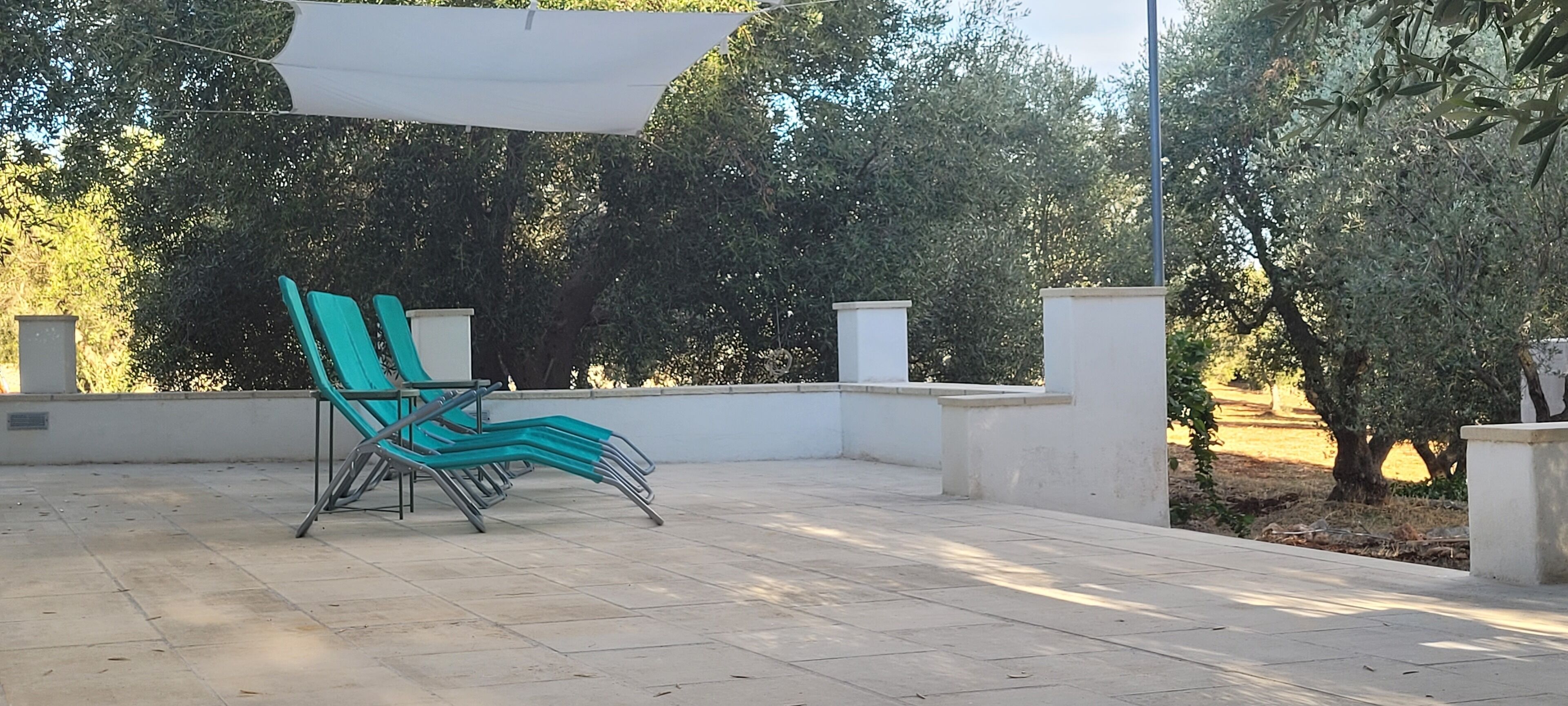 Un área de estar al aire libre techada, con una única silla turquesa y una vela de sombra blanca por encima.