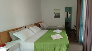 Une chambre d’hôtel avec un lit, un bureau, une chaise, un tableau accroché au mur et une salle de bain visible à travers une porte ouverte.