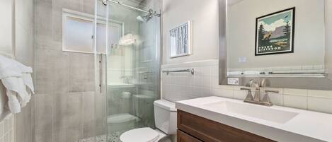 A modern bathroom with a glass-enclosed shower, a white toilet, and a vanity with a large mirror.