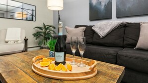 A living room with a wooden coffee table, a bottle of wine, glasses, and orange slices. - Peterson Flats Urban Group Getaway (Fort Collins)