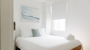 A bedroom with a bed, white bedding, a single pillow, a window, and a painting on the wall.