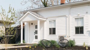 A white house with a porch, two outdoor chairs, and a garden with young plants.