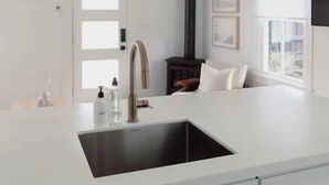A modern kitchen with a white countertop, a black sink, and a wooden stove.