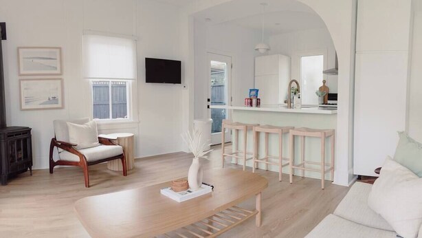 A modern living room with a wooden coffee table, a white sofa, and a kitchen area visible through an archway.