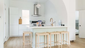 A modern kitchen with a central island, wooden stools, and a large window.