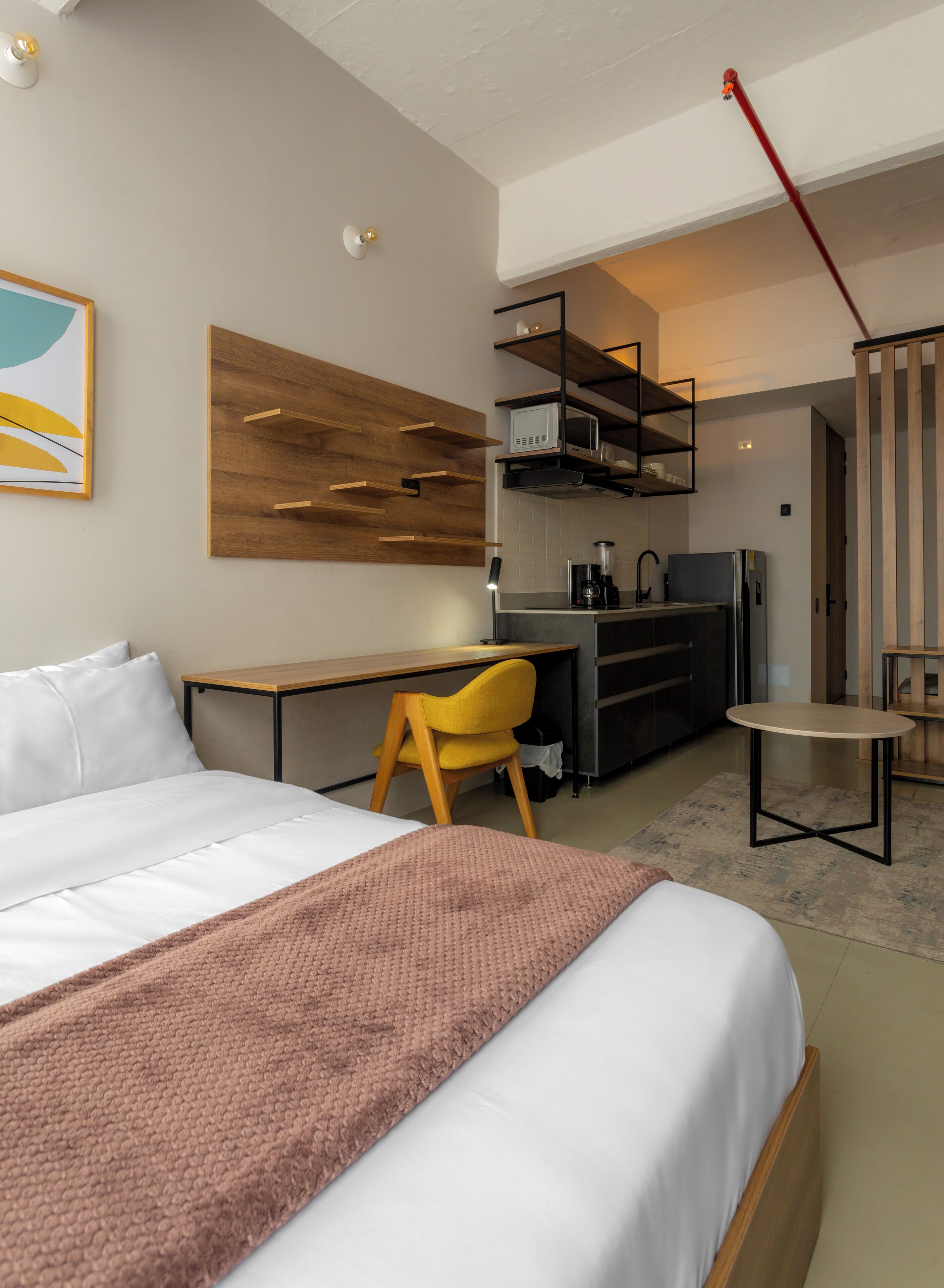 Una habitación de hotel moderna con cama, escritorio, silla, pequeña cocina y mesa de comedor.