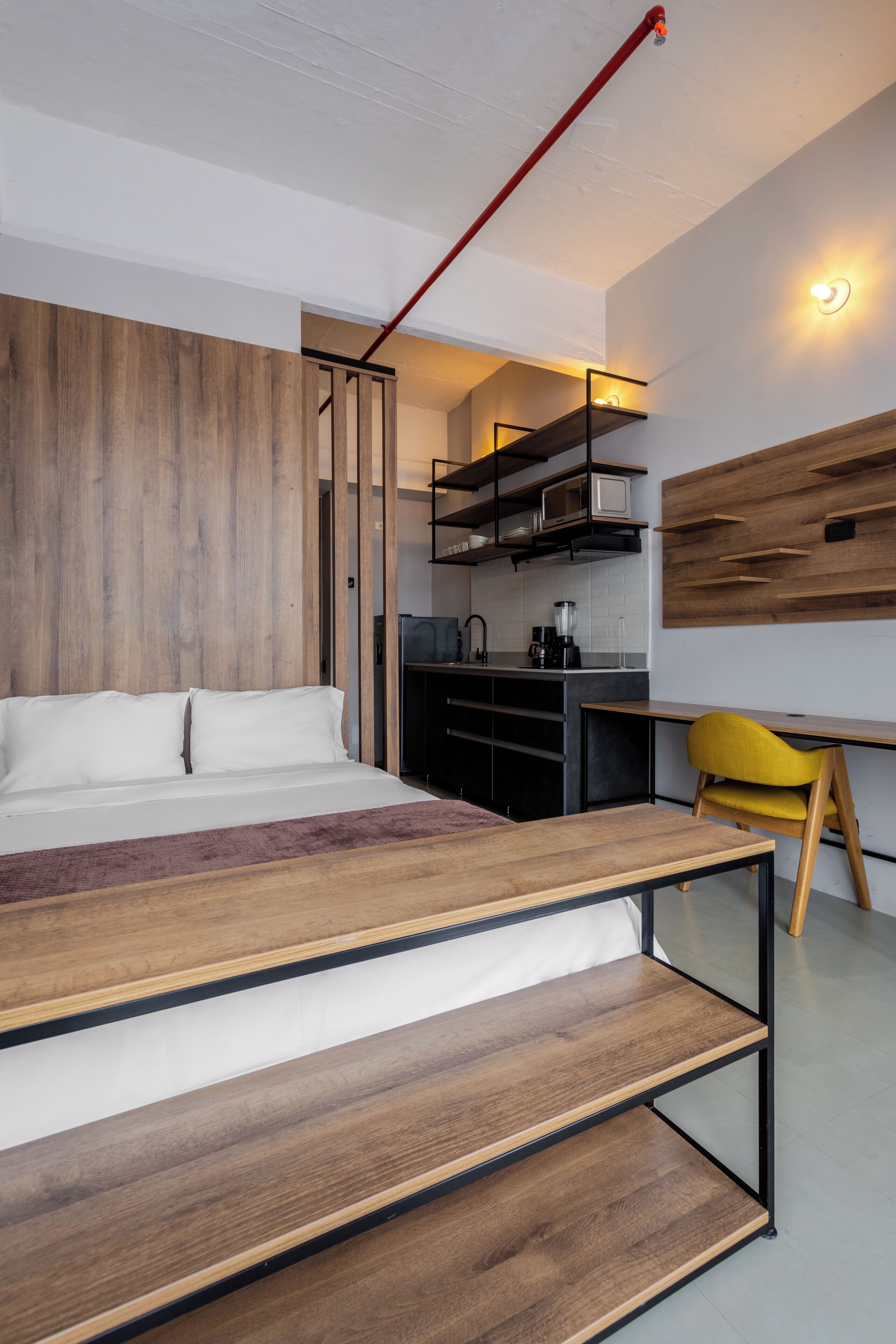 Un dormitorio moderno con cama, plataforma de madera y un espacio de escritorio con una silla.