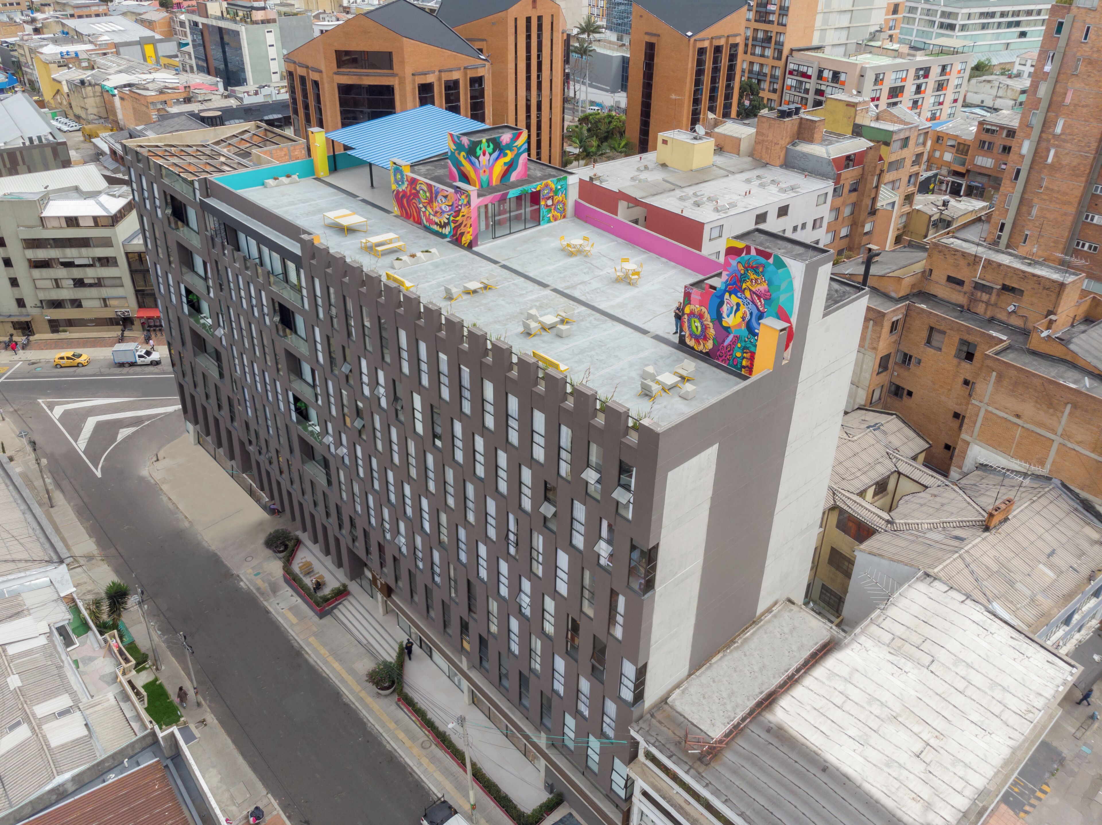 A high-rise building with a rooftop terrace featuring outdoor seating and a colorful mural.