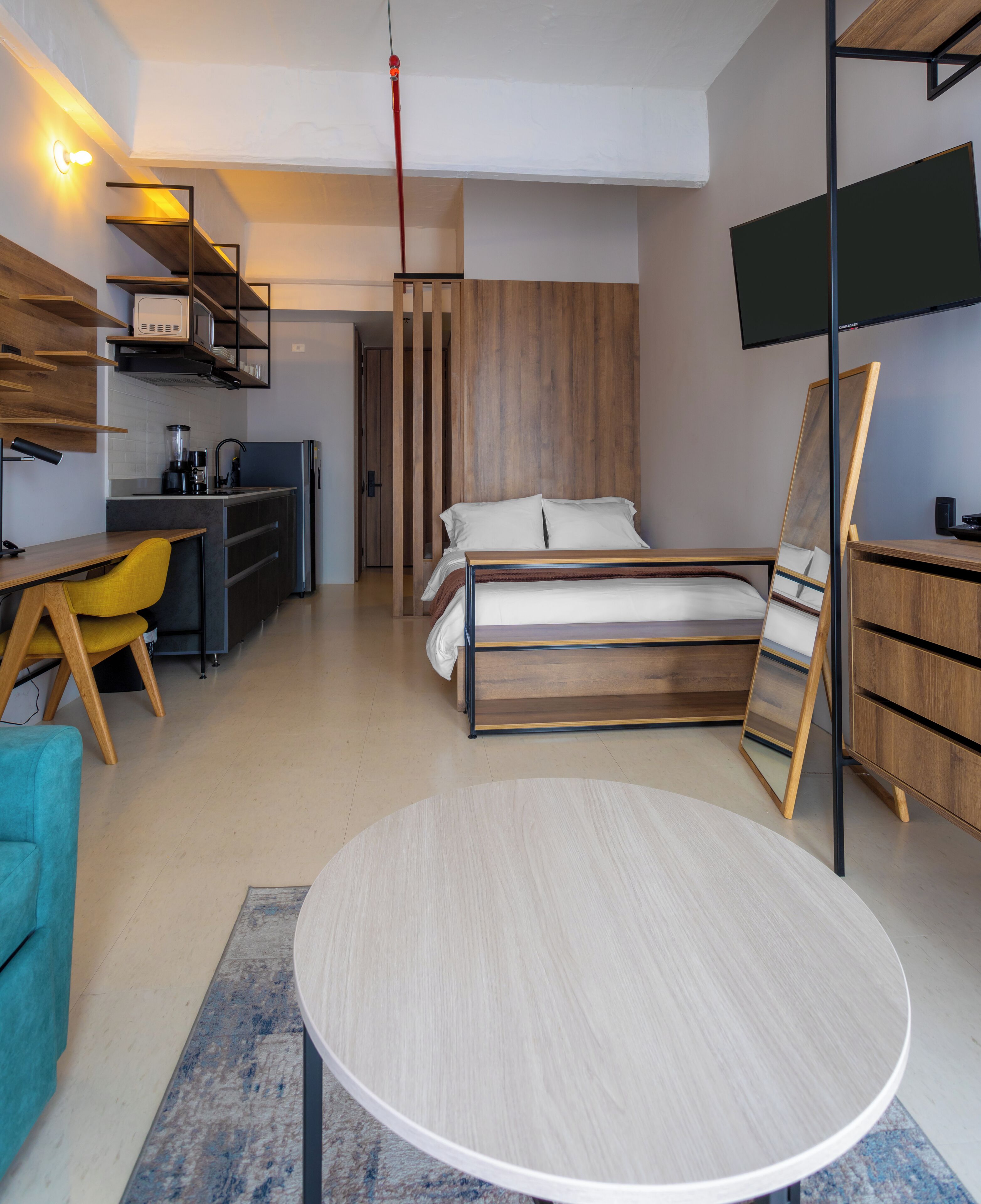 A modern hotel room with a bed, a desk, a chair, a TV, and a wardrobe.