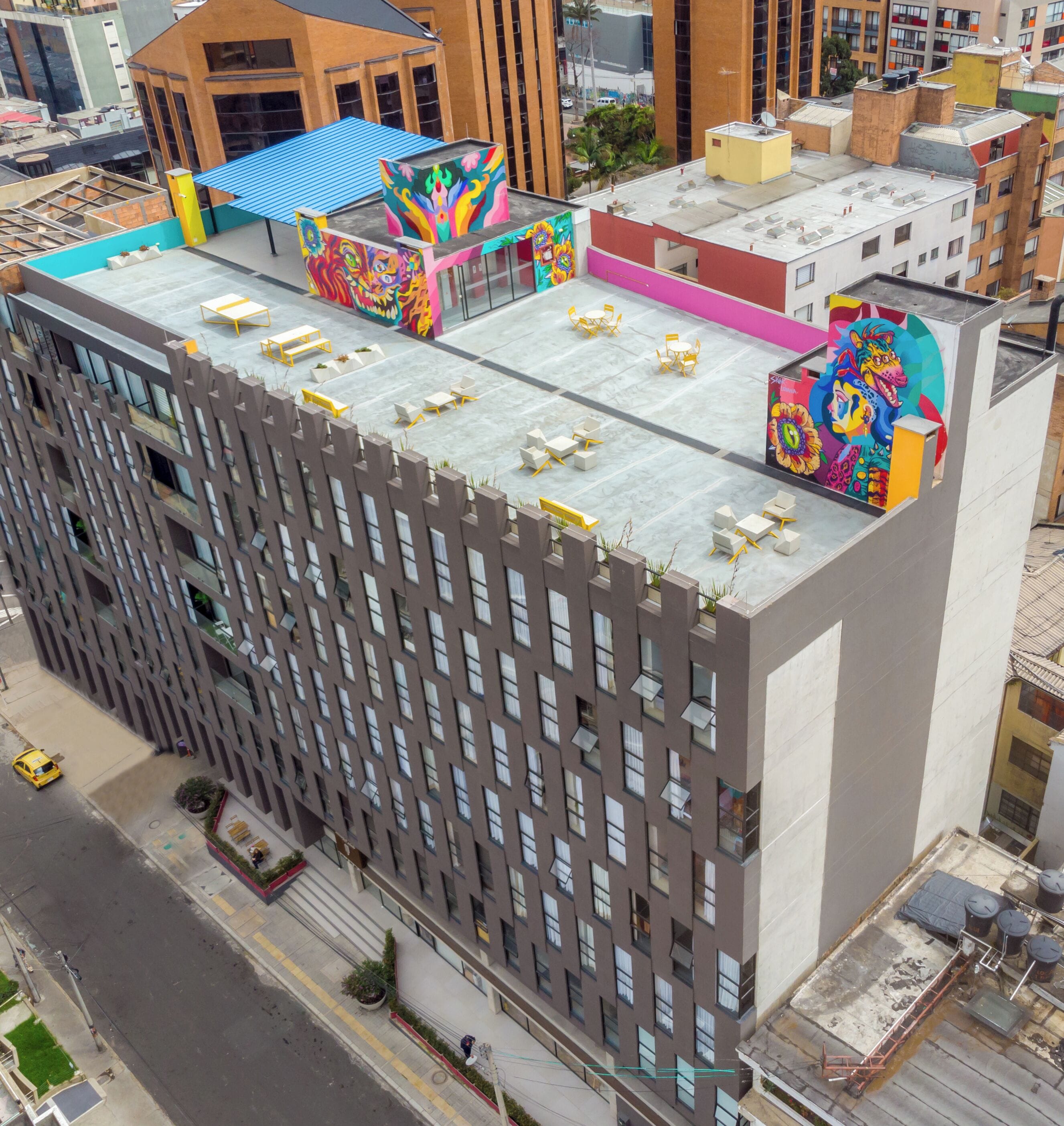 A multi-story building with a flat roof, multiple balconies, and a rooftop terrace with outdoor seating.