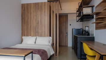 A modern hotel room with a bed, a desk, and a kitchenette.