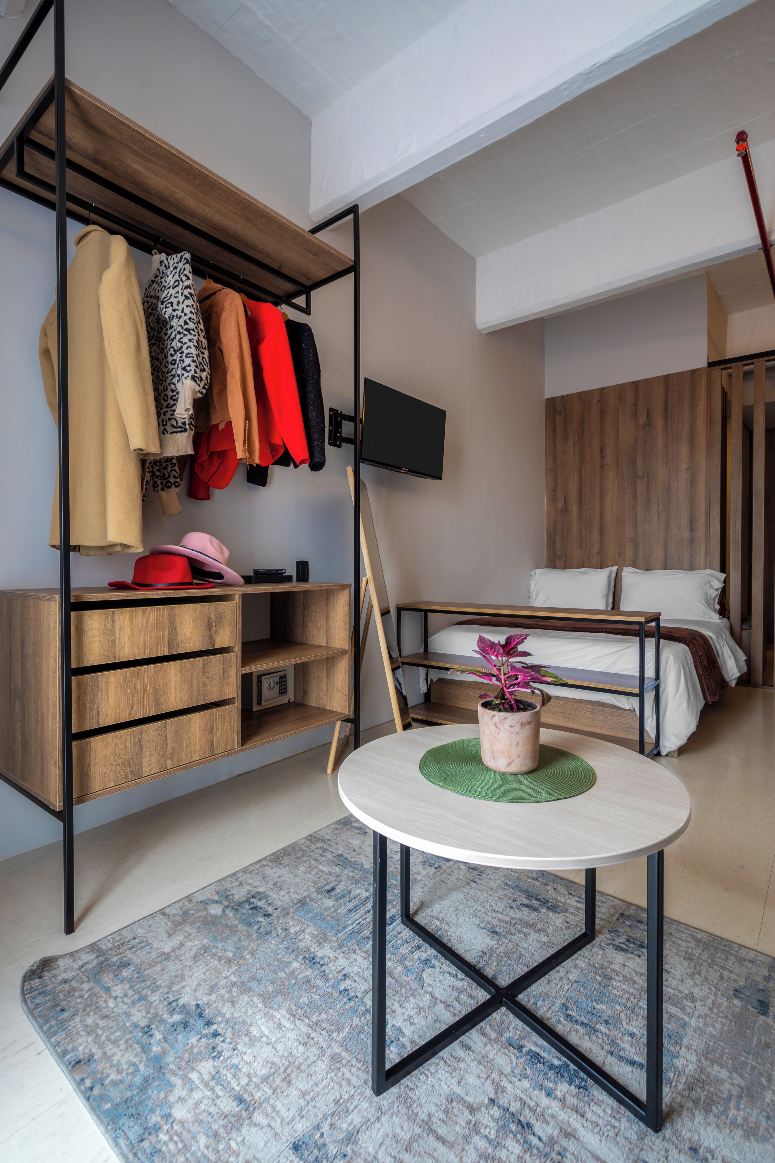 Ein modernes Schlafzimmer mit einem Holzschrank, einem Bett, einem kleinen Tisch mit einer Pflanze und einem an der Wand befestigten Fernseher.