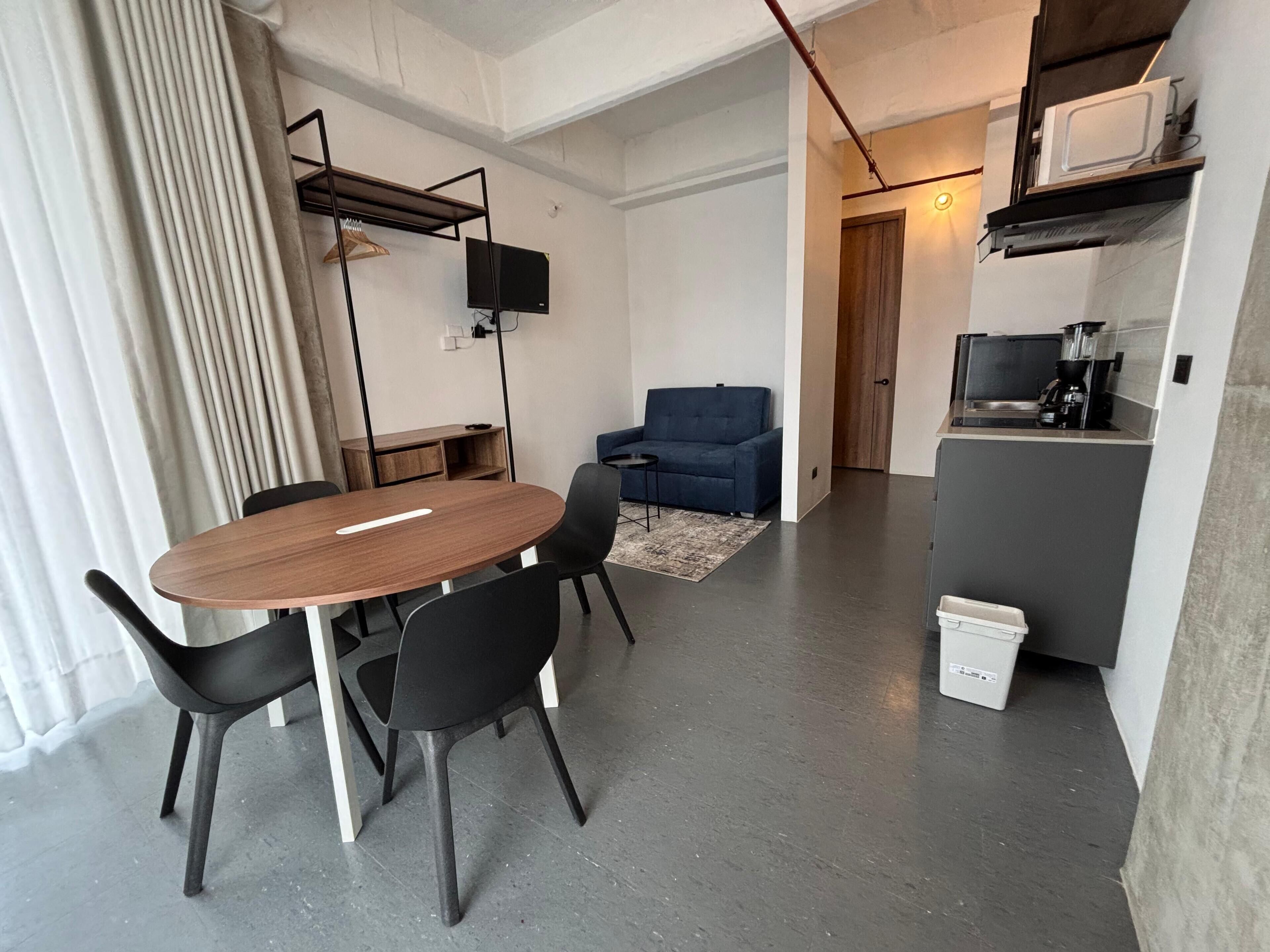 A modern living space with a dining area, a sofa, a kitchen, and a TV.