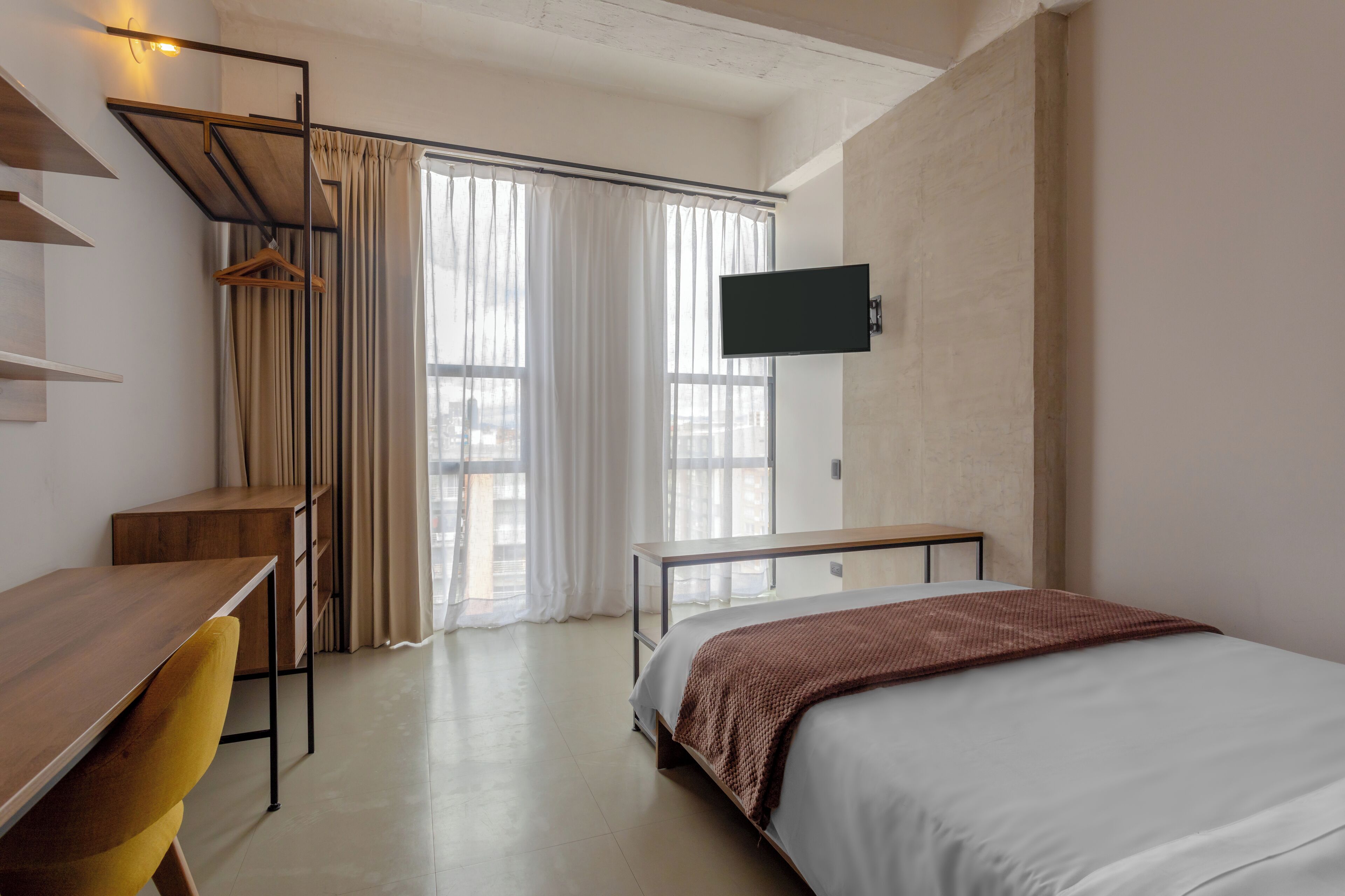 Une chambre d’hôtel moderne équipée d’un lit, d’un bureau, d’une chaise, d’une télévision et d’une fenêtre avec des rideaux.