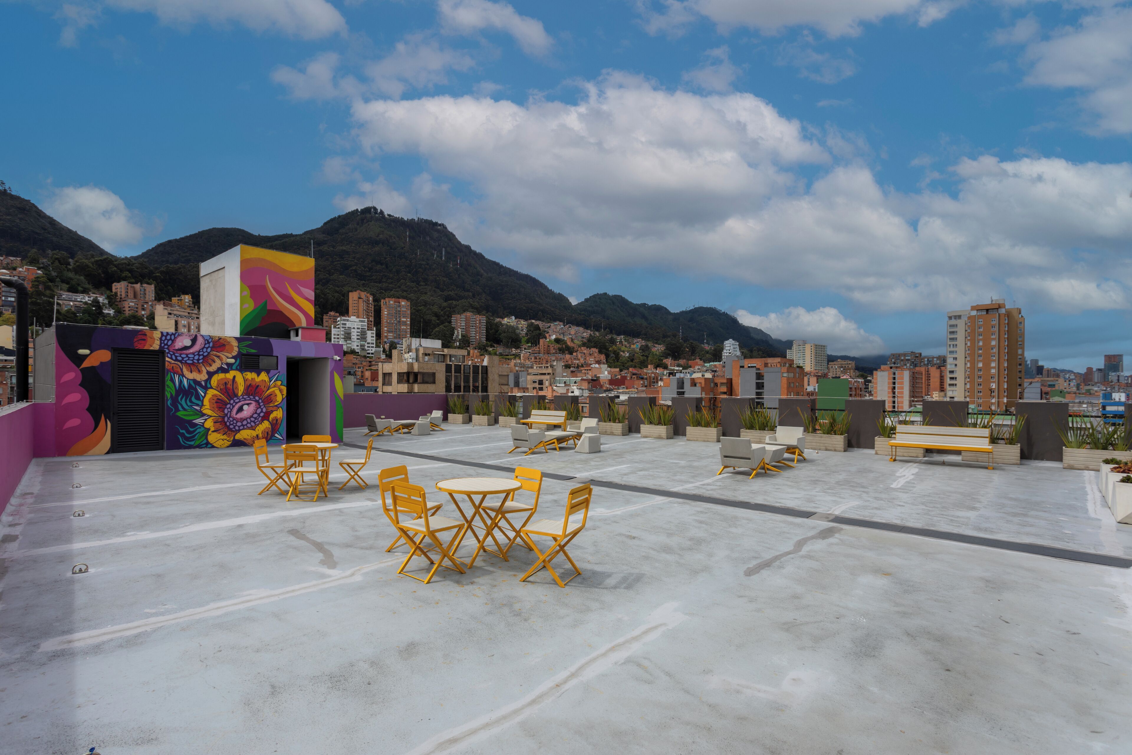 Terraço no telhado com área de estar ao ar livre, um mural colorido e vista para a cidade com montanhas ao fundo.