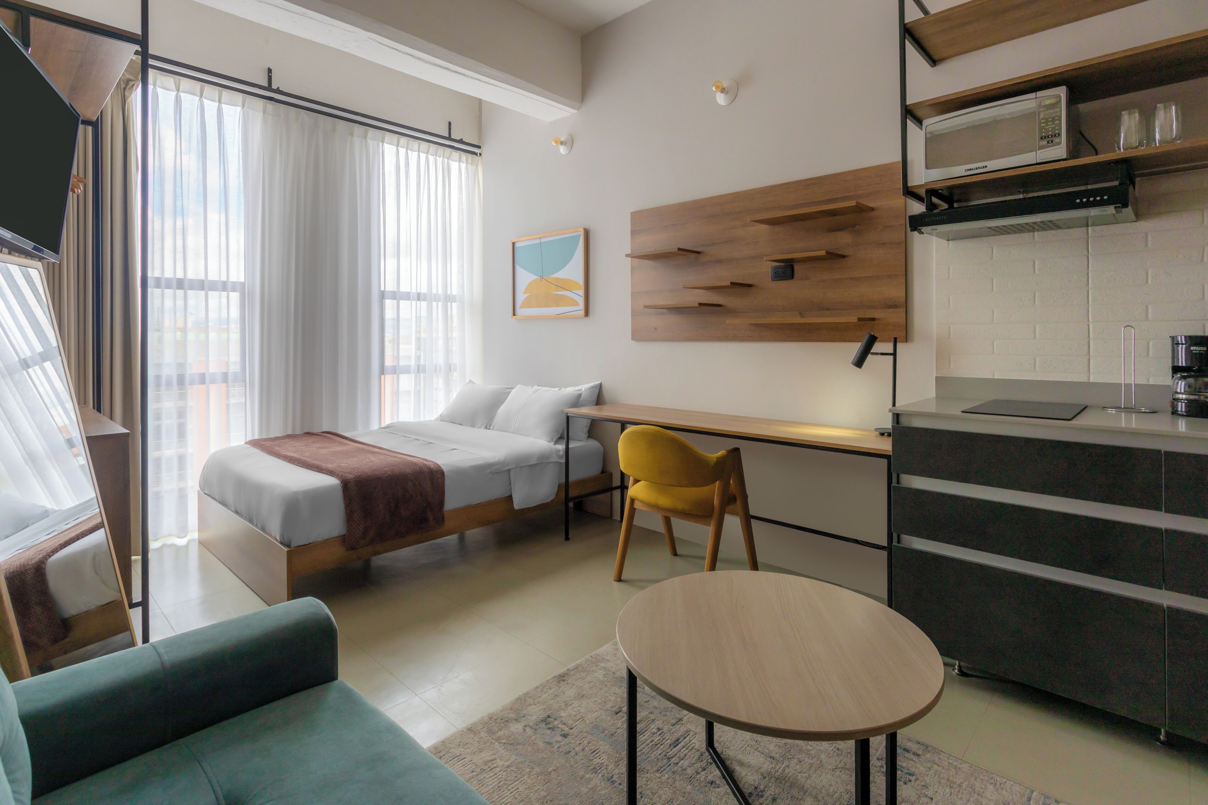 Ein modernes Hotelzimmer mit Bett, einer Sitzecke, einem Esstisch und einer Küchenzeile.