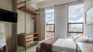 A modern hotel room with a bed, a desk, a wardrobe, and a large window offering a city view. - Ivin 567 by Atelier (Bogotá)
