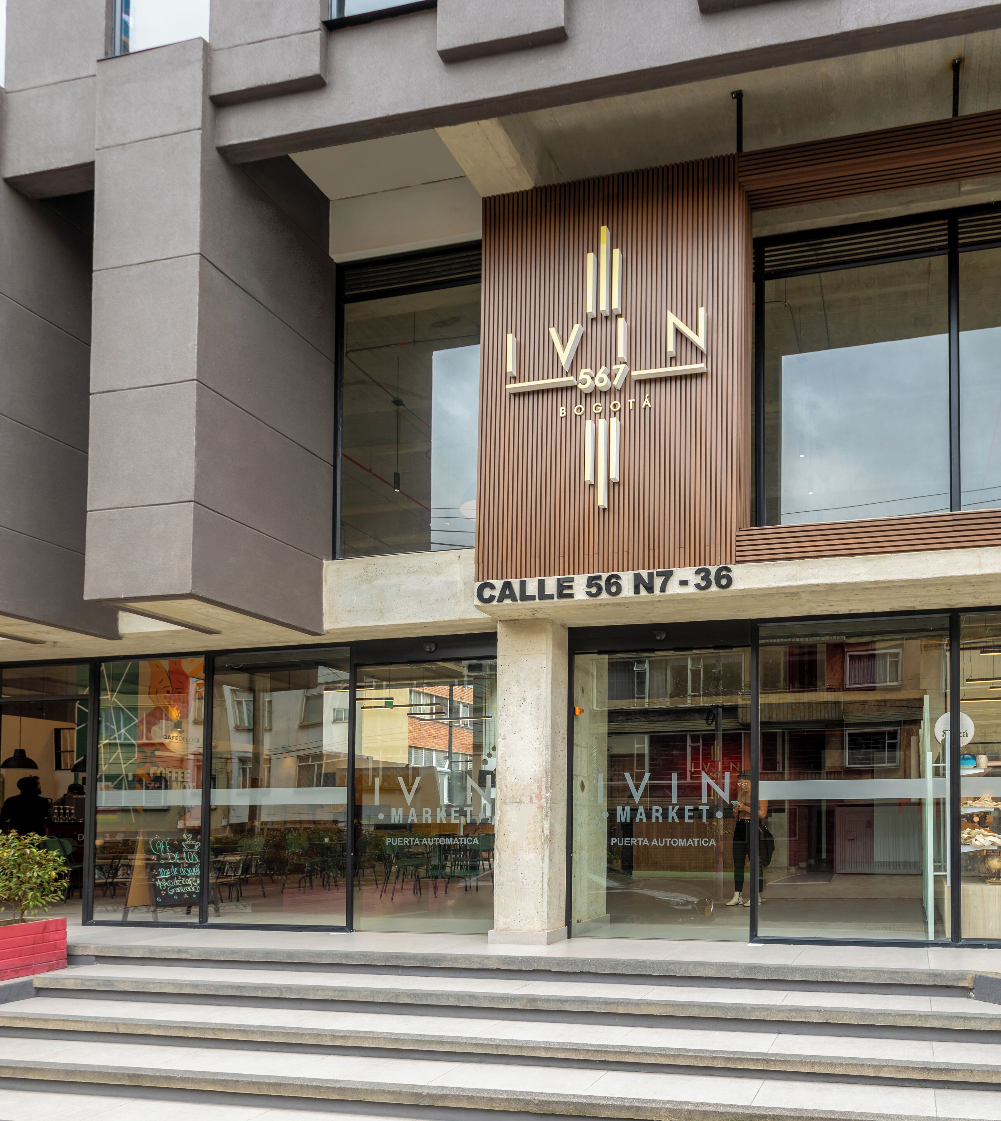 A modern building with a prominent 'IVIN MARKET' sign, featuring a vertical design with the number '567' and 'BOGOTA' below. The entrance has glass doors and a visible street name 'Calle 56 N7-36'.