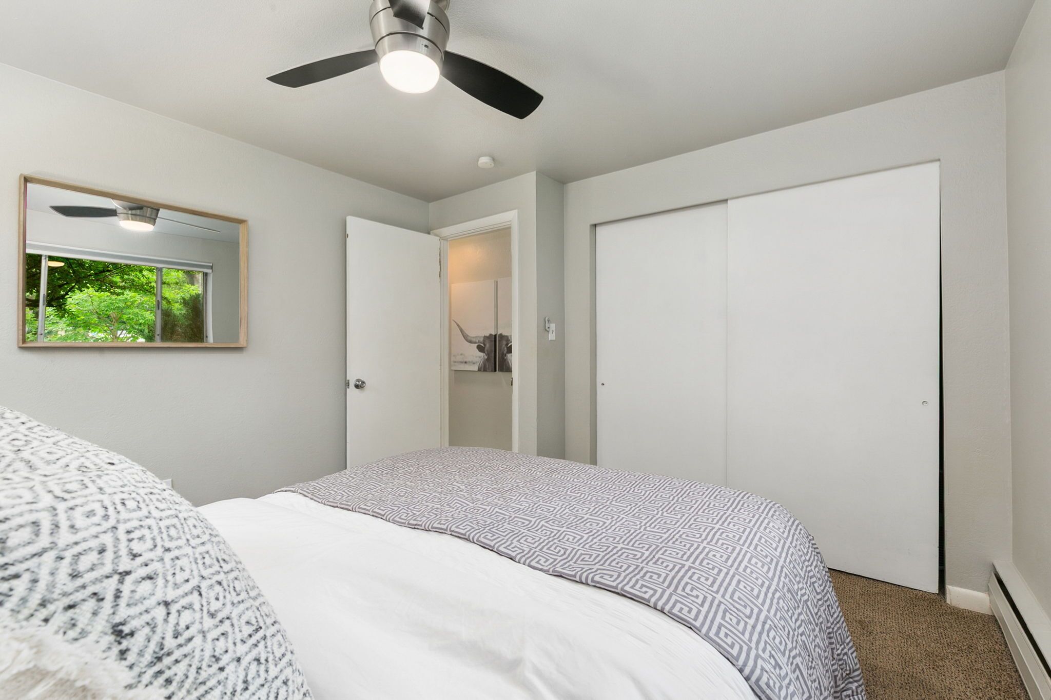 A bedroom with a bed, a ceiling fan, a mirror, and a closet.