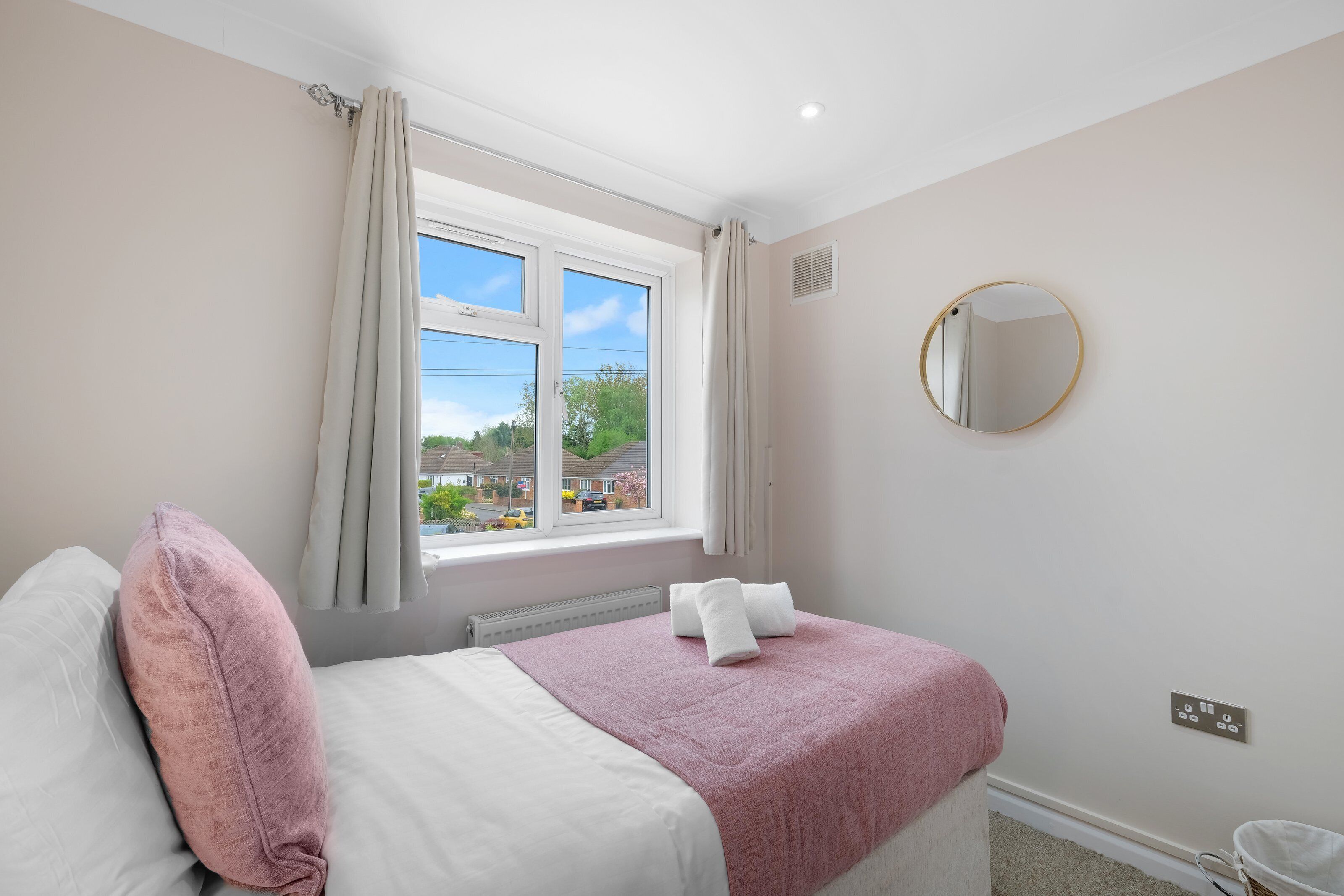 A bedroom with a bed, a window, a round mirror, and a radiator.