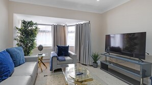 Uma sala de estar moderna com sofá, mesa de centro, TV em um suporte e uma janela grande com cortinas.