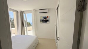 Et hotelværelse med en seng, en aircondition, et vindue med gardiner og en dør med håndtag.