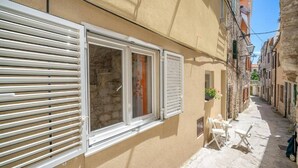 Eine enge Straße mit Gebäuden, einem Fenster mit Rollläden und Gartenmöbeln.