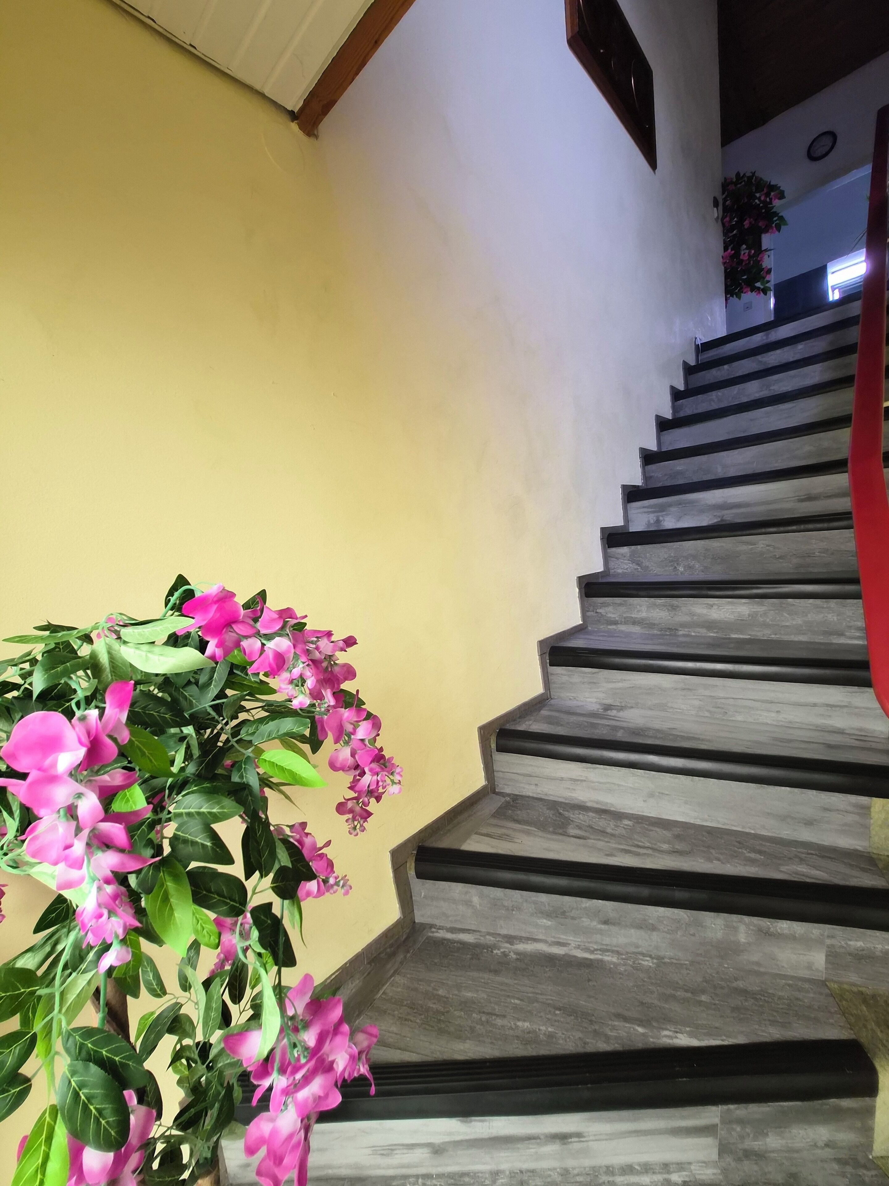 Una escalera de madera con peldaños y una planta con flores rosadas sujeta a la pared.