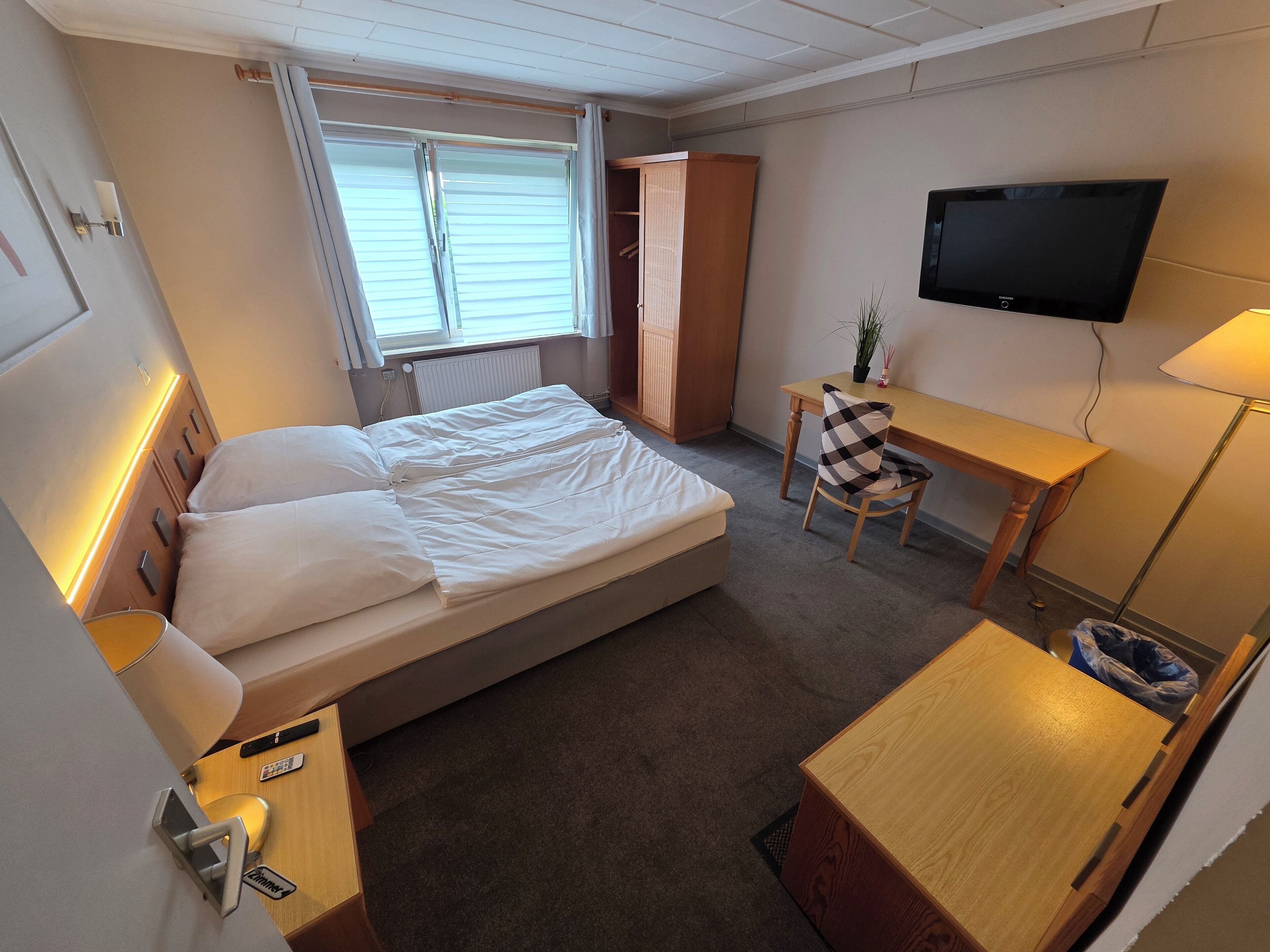 A hotel room with a bed, a desk, a chair, a TV, and a wardrobe.