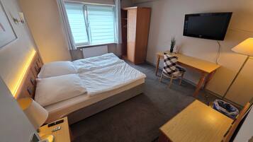 A hotel room with a bed, a desk, a chair, a TV, and a wardrobe.