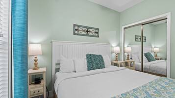 Un dormitorio ordenado con una cama, mesitas de noche, lámparas y un espejo.