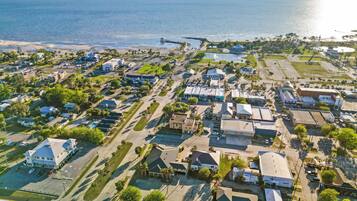 Vista aérea de un pueblo costero con casas residenciales, un muelle que se adentra en el mar y una vista despejada del océano.
