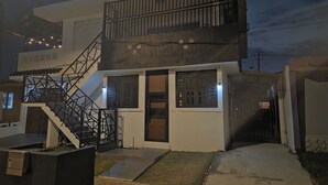 Un edificio de dos pisos con una escalera, un acceso con puerta y un pequeño espacio exterior con escalones que conducen a la entrada.