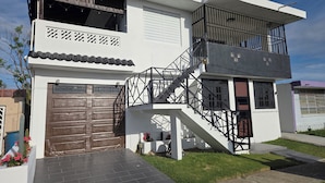 Una casa moderna de dos pisos con una puerta de garaje marrón, una escalera con barandillas negras y un pequeño jardín.
