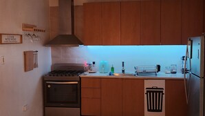 Una cocina compacta con armarios de madera, un refrigerador de acero inoxidable, una estufa y un lavamanos.