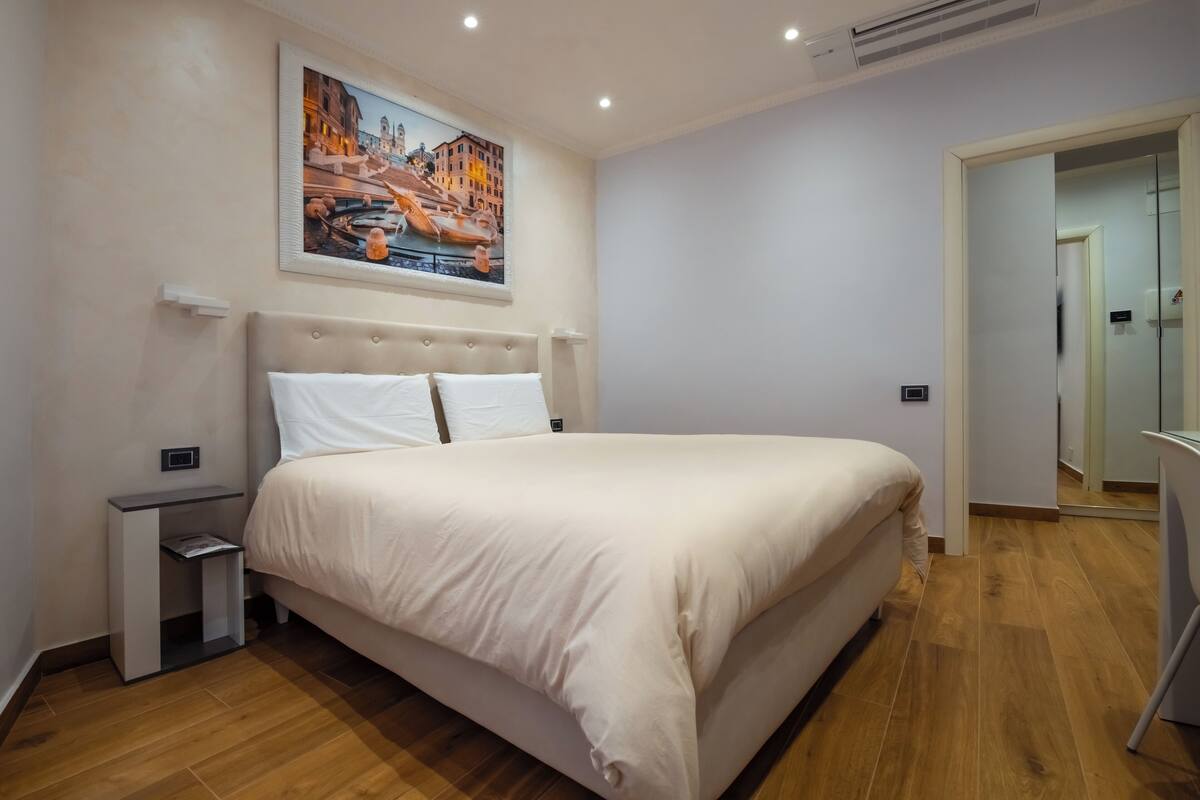 A bedroom with a bed, bedside tables, a painting, and a wooden floor.