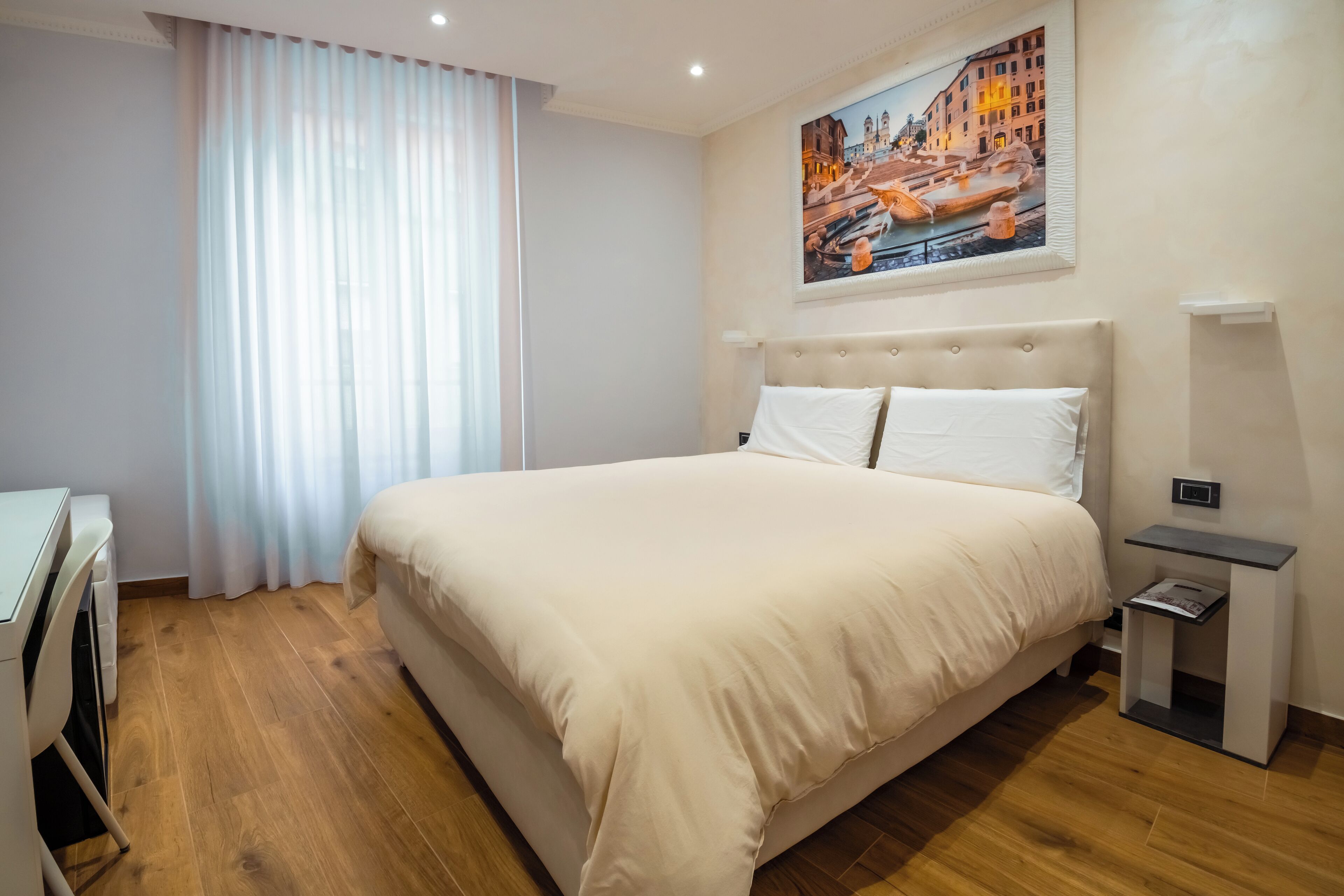 A neatly arranged hotel room with a large bed, a desk, and a painting of a cityscape on the wall.