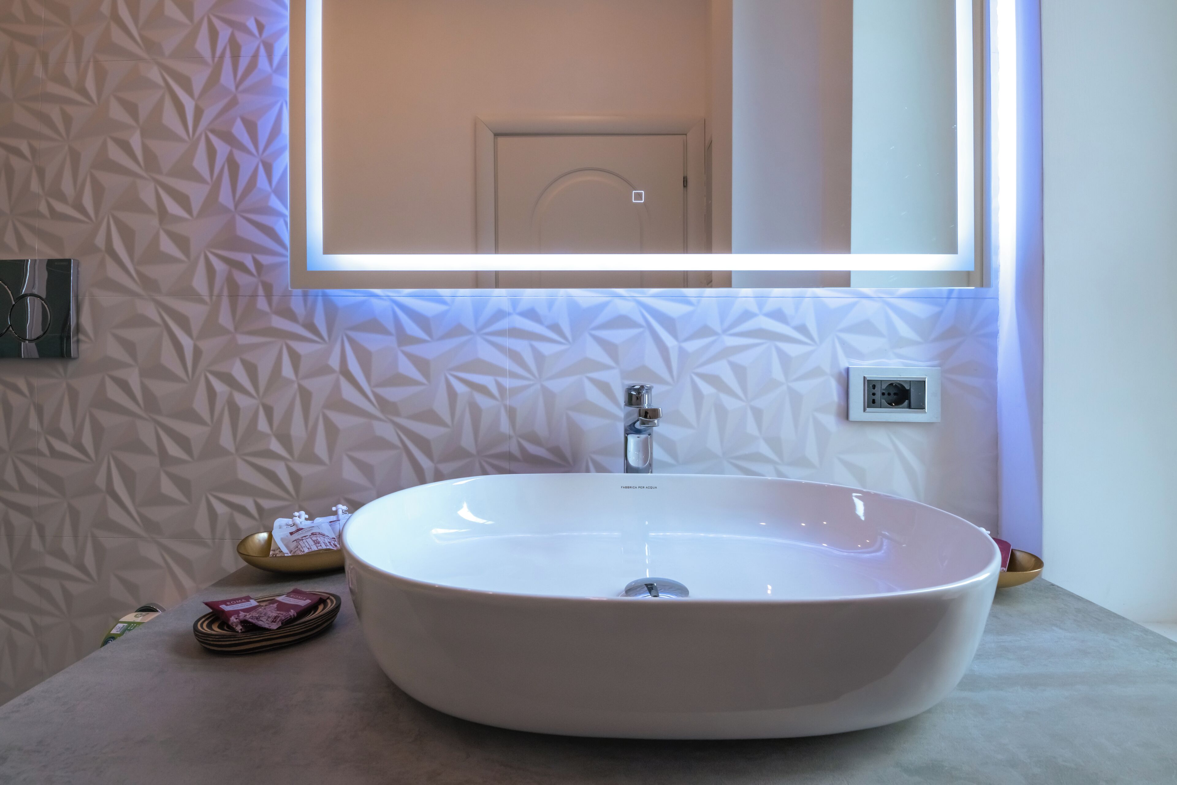A bathroom with a large oval sink, a mirror above it, and a geometric patterned wall.